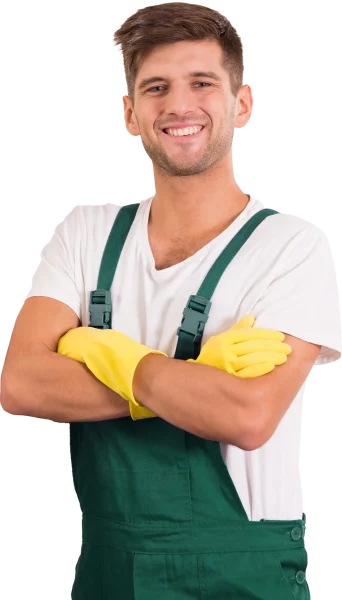 A smiling man wearing a white t-shirt, green overalls, and yellow rubber gloves stands with his arms crossed.